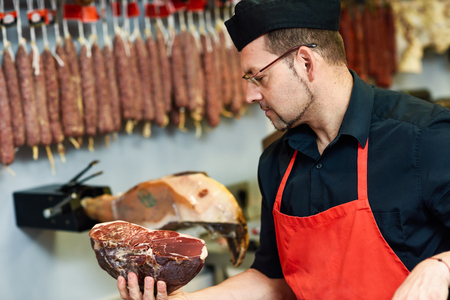 Butcher with a piece of ham in his hand inside a butcher shopの写真素材