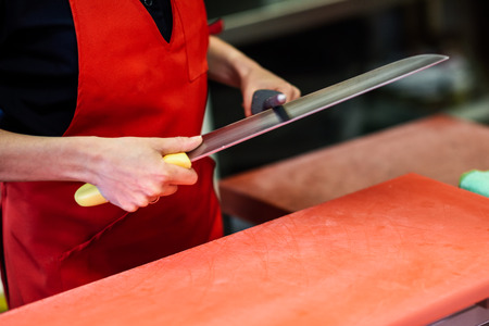 Young female butcher sharpening a knife in a butcher shopの写真素材