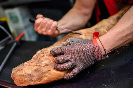 Close-up of butcher boning a ham in a modern butcher shop with metal safety mesh gloveの写真素材