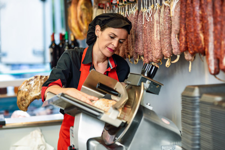 Female butcher cutting york ham in a cutting machine inside a butcher shop.の写真素材