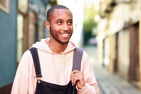 Young black man wearing casual clothes walking smiling down the street. Millennial african guy with bib pants outdoorsの写真素材