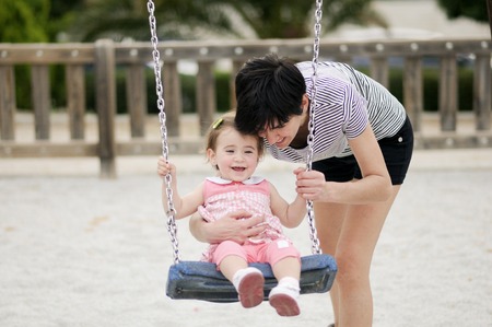 Mother swinging her little daughter on a swingの写真素材