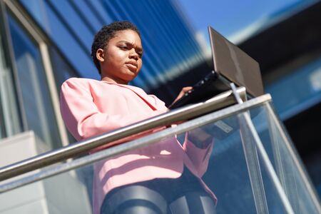 Black businesswoman standing near business office building working with a laptop computer.の写真素材
