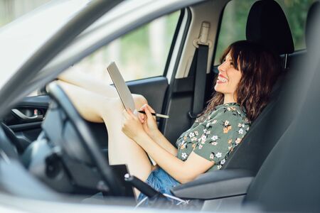 Woman writing in a notebook with a pen in a white carの写真素材