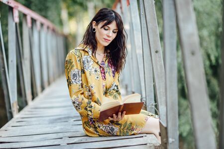 Young woman reading a book on a rural bridge.