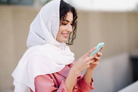 Young Muslim woman wearing hijab texting message with her smartphone.の写真素材