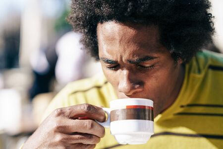 Black man enjoying coffee in cafe while sitting at the table outdoorsの写真素材