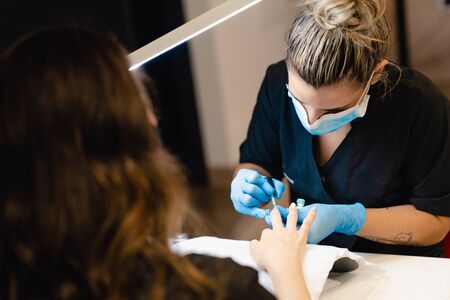 Close-up of Beautician painting her clients nails in blue and yellow nail varnish.の写真素材