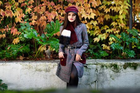 Young beautiful girl with very long hair wearing winter coat and cap in autumn leaves background