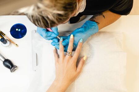 Close-up of Beautician painting her client's nails in blue and yellow nail varnish in a beauty centreの写真素材