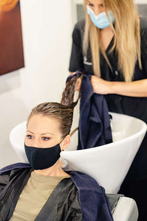 Female hairdresser washing a clients head in a salon, protected by a maskの写真素材