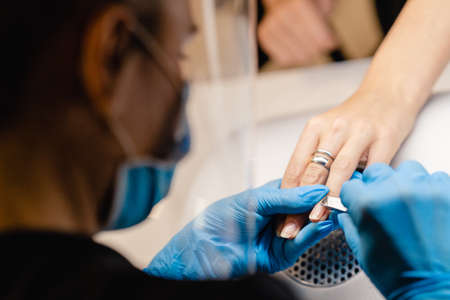 Aesthetician doing the manicure, filing the nails with a file to his client in a beauty center