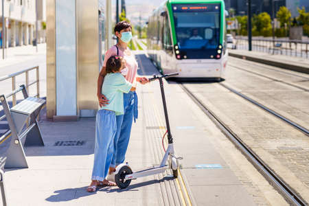 Mother and daughter waiting for the train with an electronic scooter.の写真素材