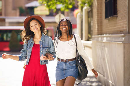 Two female walking together on the street. Multiethnic friends.の写真素材