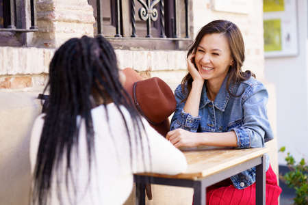 Two multiethnic friends talking sitting at a table outside a bar.の写真素材
