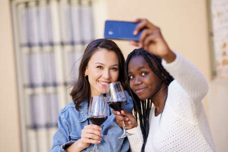 Two women making a selfie with a smartphone while having a glass of wine.の写真素材