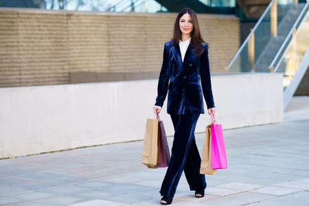 Young woman wearing blue suit carrying several shopping bags near a shopping mall.の写真素材