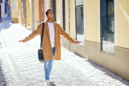 Young black man walking down the street carrying a briefcase and a smartphone.の写真素材