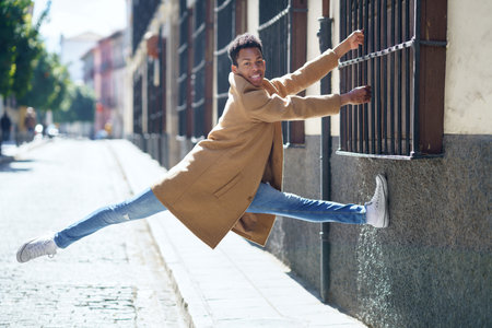 Young Cuban man jumping holding on to a window grille in the street.の写真素材