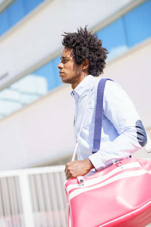 Black worker walking near an office building with a sports bag.の写真素材
