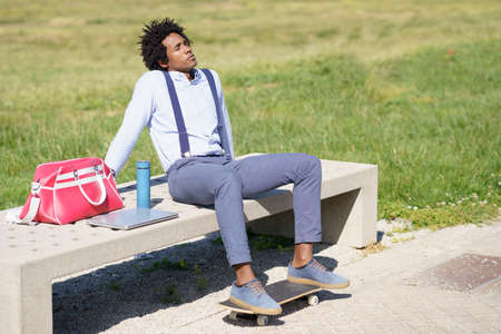 Black man with afro hair taking a coffee break sitting on a park bench.の写真素材