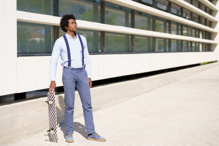 Black male worker standing next to an office building with a skateboard.の写真素材
