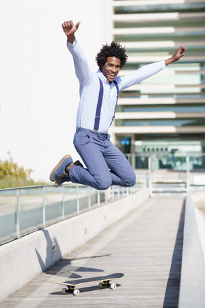 Black businessman jumping on a skateboard near an office building.の写真素材