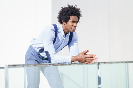 Attractive black businessman with afro hair, resting on a railing of his office building.の写真素材