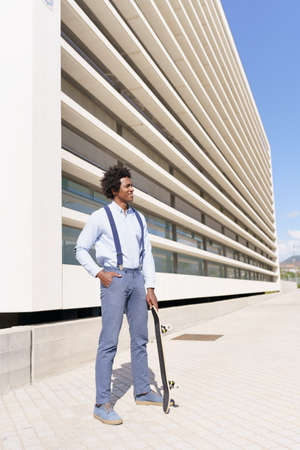 Black male worker standing next to an office building with a skateboard.の写真素材