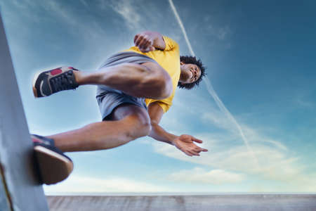 View from below of black man jumping on his run.の写真素材