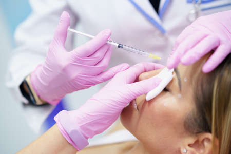 Aesthetic doctor injecting vitamin into the forehead of her middle-aged patient.