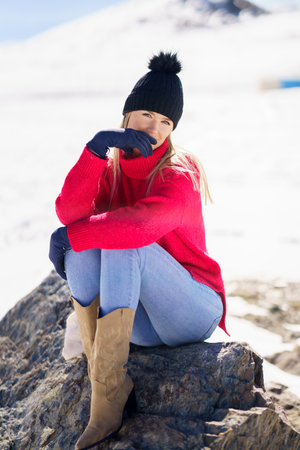 Young woman sitting on a rock in the snowy mountains in winter, in Sierra Nevada, Granada, Spain.の写真素材