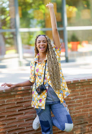 Black female with African braids, raising her arm in joy. Girl holding a camera.の写真素材