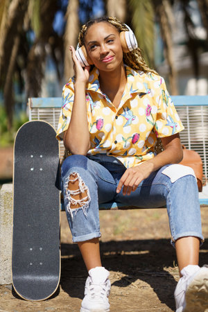 African woman with skateboard relaxing after riding skateboard listening to the musicの写真素材