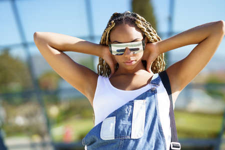 Black woman dressed casual, looking at camera with modern sunglasses.