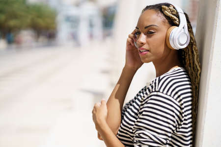 Young black woman listening to music with wireless headphones outdoors.
