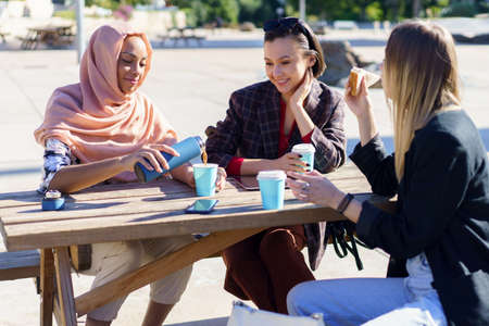 Positive diverse women having coffee break at table in parkの写真素材