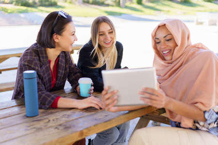 Cheerful diverse ladies sharing tablet during coffee break in cafeの写真素材