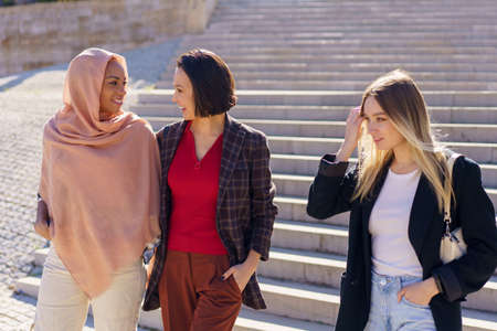 Positive young diverse female friends walking downstairs in campusの写真素材