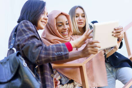 Smiling young diverse ladies using tablet on stairsの写真素材