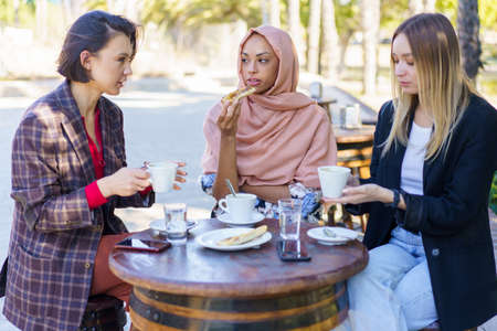 Young diverse ladies drinking coffee in street cafeの写真素材