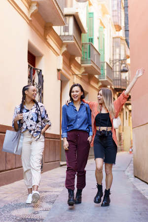 Satisfied young diverse women walking in old city district and laughingの写真素材
