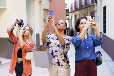 Stylish young diverse women taking photos during vacation in old cityの写真素材