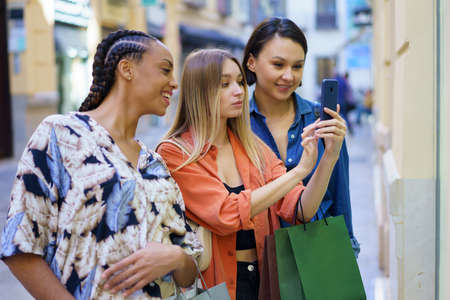 Fashionable multiracial ladies taking photo on smartphone during shopping in cityの写真素材