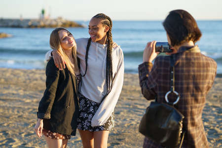 Woman taking photo of diverse girlfriends on beachの写真素材
