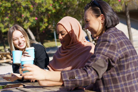 Cheerful young multiracial female coworkers laughing and communicating while having coffee break...
