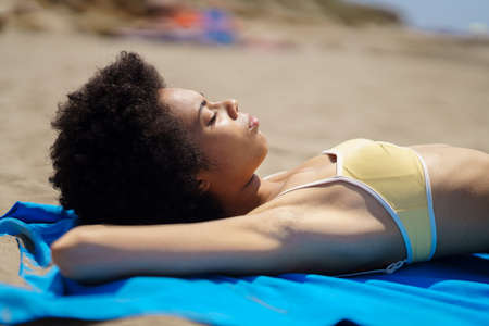 Relaxed black woman lying on the sand of a tropical beach sunbathing. African American girl tanning.