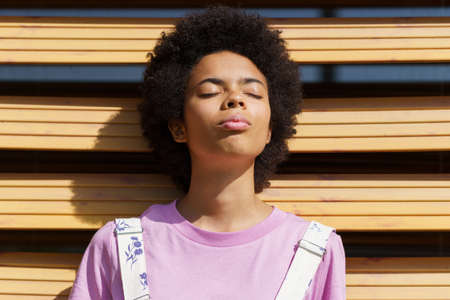 African-American woman getting sunlight on her face with her eyes closed, lost in thought, on a...