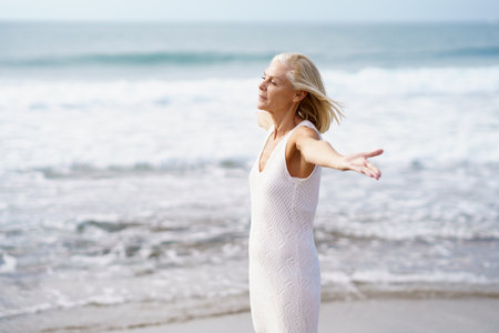 Mature female opening her arms on a tropical beach, spending her leisure time. Elderly woman enjoying her retirement at a seaside retreat.の写真素材