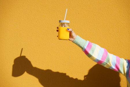 Female hands holding a glass tumbler with lid and straw, to take away, filled with fresh orange...